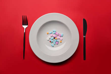Supplements as food on round white plate with fork and knife. Concept of vitamins instead of food.の写真素材