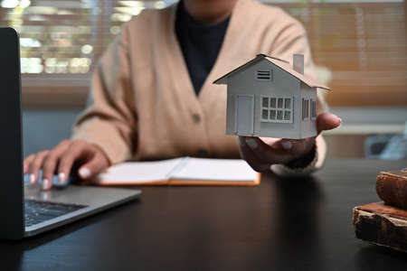 Woman using laptop computer and showing house model. Mortgage and real estate investment concept.の写真素材