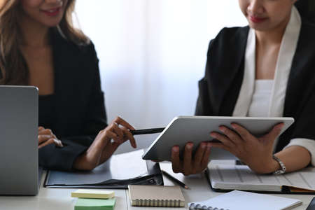 Two smiling young businesswomen analyzing financial data on digital tablet together.