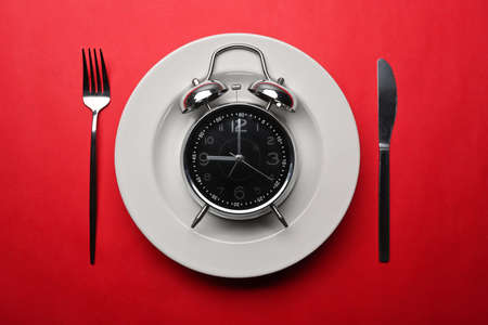 Alarm clock with knife and fork on red background. Meal planning for diet concept.の写真素材