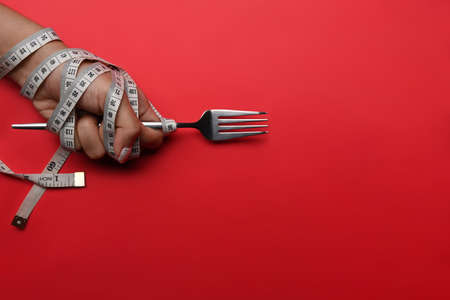 Woman hand holding fork with measuring tape on red background. Loss weight and healthy diet concept.の写真素材
