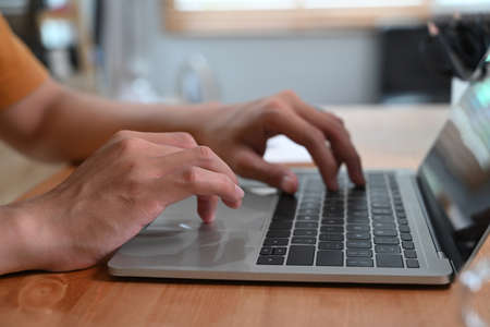 Close up view man typing on keyboard of laptop computer.