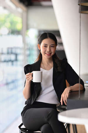 Portrait of confident asian businesswoman sitting in modern office and drinking coffee.の写真素材