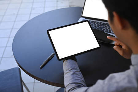 View over shoulder businessman sitting in front of laptop and using digital tablet.