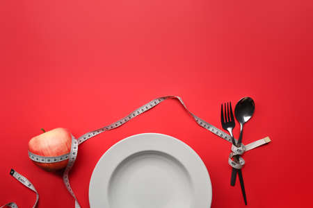 Loss weight and healthy diet concept. Fork with measuring tape on red background. Copy space for text.の写真素材