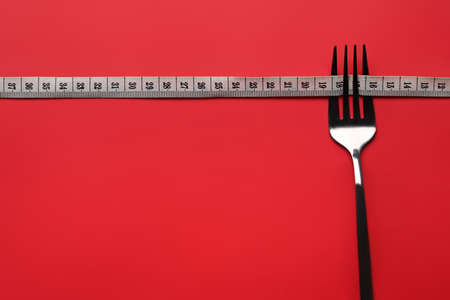 Loss weight and healthy diet concept. Fork with measuring tape on red background. Copy space for...