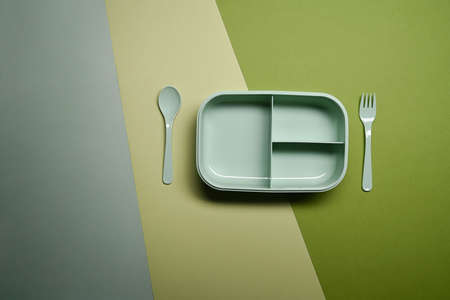 Empty lunch box with spoon and fork on green background.の写真素材