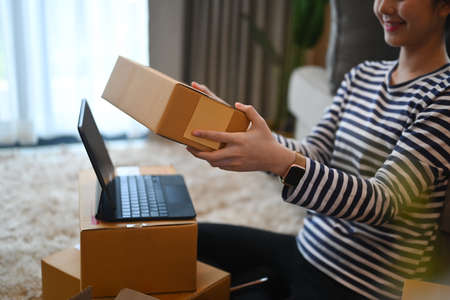 Smiling young woman online seller preparing parcel box of product for delivery to customer.
