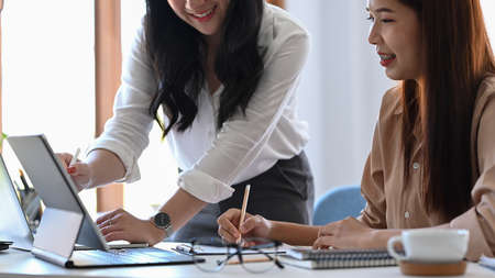 Cheerful businesswoman sitting at office with her colleague and talking on mobile phone.