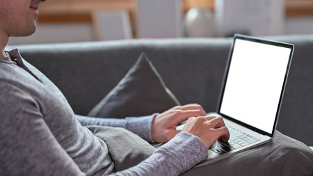 Young man in casual clothes sitting on sofa and working with laptop computer.の写真素材