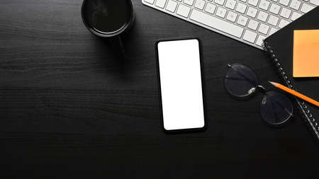 Top view smart phone with blank screen, laptop computer and supplies on black table.の写真素材