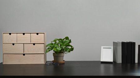 Small wooden drawer, houseplant, books and picture frame on black table.