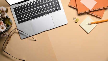 Above view laptop computer, notebook, glasses and calculator on beige background.