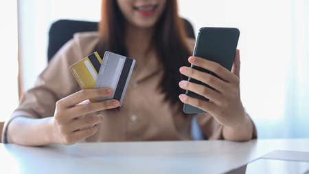 Smiling asian woman holding credit card and shopping online on her smart phone.の写真素材