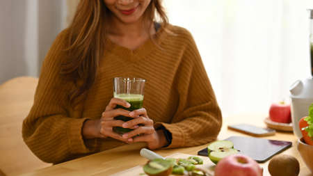 Smiling asian woman making detox smoothie with blender in kitchen.