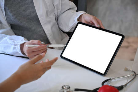 Close up view doctor in white medical uniform using digital tablet and giving advice to patient.の写真素材