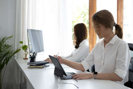Young businesswoman working with computer tablet while sitting with her colleague in office.