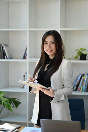 Smiling businesswoman sitting in front of laptop computer at office desk and talking on mobile...