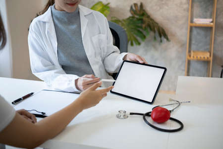 Friendly female doctor using digital tablet and explaining, discussing medical checkup result to patient.の写真素材