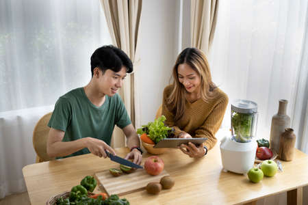 Healthy young couple preparing ingredients for making green vegetables detox smoothie in kitchen.の写真素材