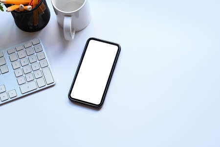 Top view mockup smart phone, coffee cup and pencil holder on white office desk.の写真素材