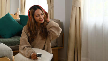 Peaceful asian woman reading book and drinking coffee on sofa.