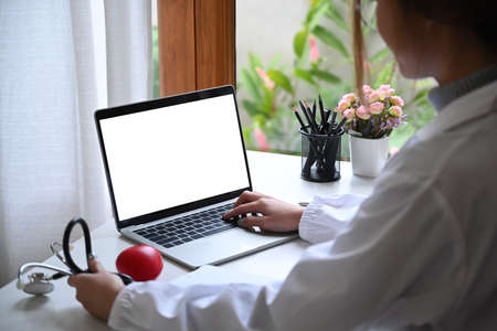 Female doctor in white uniform working with laptop computer at medical office.の写真素材