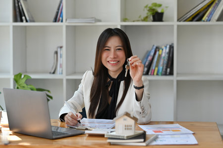 Real estate agent holding house key in hand and smiling at camera. Real estate investment and insurance concept.の写真素材