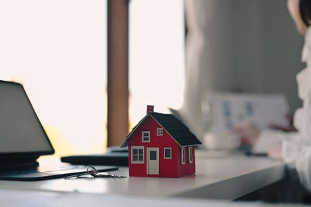 Small house model, key and computer tablet on white table. Real estate investment concept.の写真素材