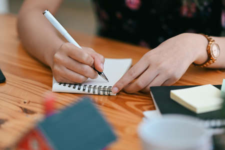 Creative woman holding pen and writing on empty notebook.