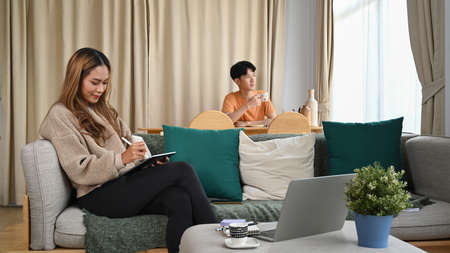 Happy young woman sitting together in living room and using digital table for shopping online.の写真素材