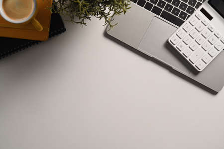 Empty notepad, pencil, laptop computer and coffee cup on white table.