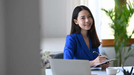 Confident business woman sitting in front of laptop computer at office desk and smiling at camera.の写真素材