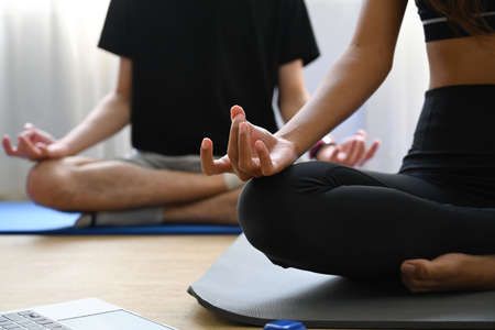 Peaceful young couple practicing yoga in lotus pose in living room.の写真素材