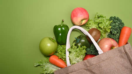 Eco bag with assorted raw organic vegetables and fruits on green background.の写真素材