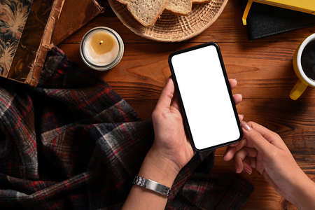 Young woman hand holding smart phone with blank screen on wooden table.の写真素材