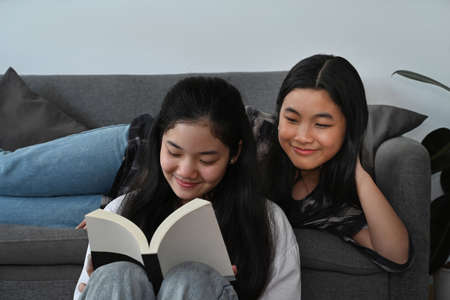 Two happy asian girls sitting in living room and reading book together.の写真素材
