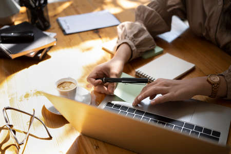 Pleased beautiful business woman reading news on laptop computer and drinking hot coffee.