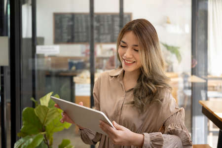 Rear view young woman sitting near glass window in coffee cup and using computer tablet.