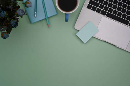 Computer laptop, coffee cup and notebook on green pastel background.