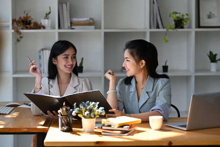 Two young asian business woman talking, advising each other at modern office.の写真素材