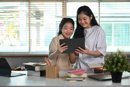 Asian girl using digital tablet with her younger sister in living room.の写真素材