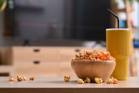 Bowl of tasty popcorn and glass on the background of home interior with a television.の写真素材