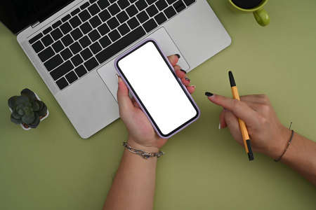 Smart phone with blank screen, laptop, notebook and coffee cup on green pastel background.