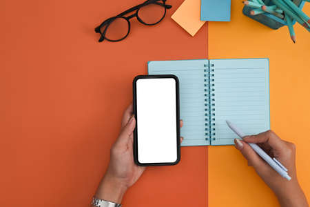 Woman hand holding mockup smart phone and making notes on notebook.の写真素材