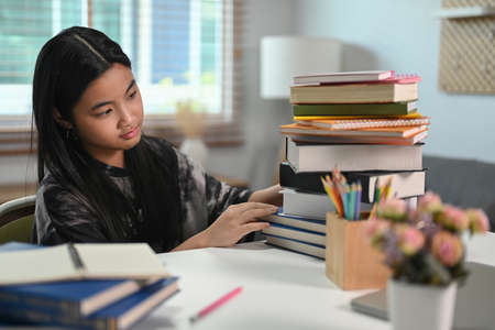 Asian elementary schoolgirl sitting with stack of books. Education concept.