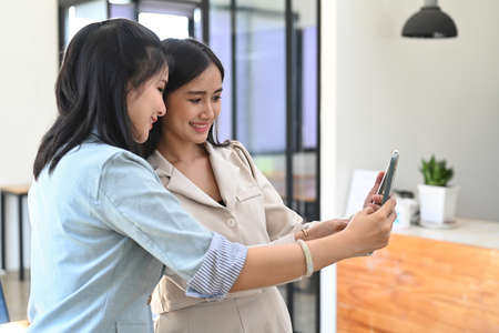 Two cheerful woman waving hand while doing video call on smart phone.