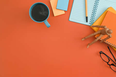 Notebook, sticky notes, eyeglasses, coffee cup on orange background. Flat lay.の写真素材