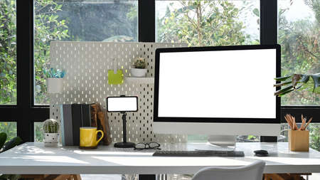 Modern workplace with computer pc, smart phone, houseplant and supplies on white table.