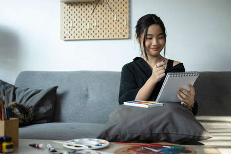 Smiling asian girl is painting picture with watercolor in living room.の写真素材